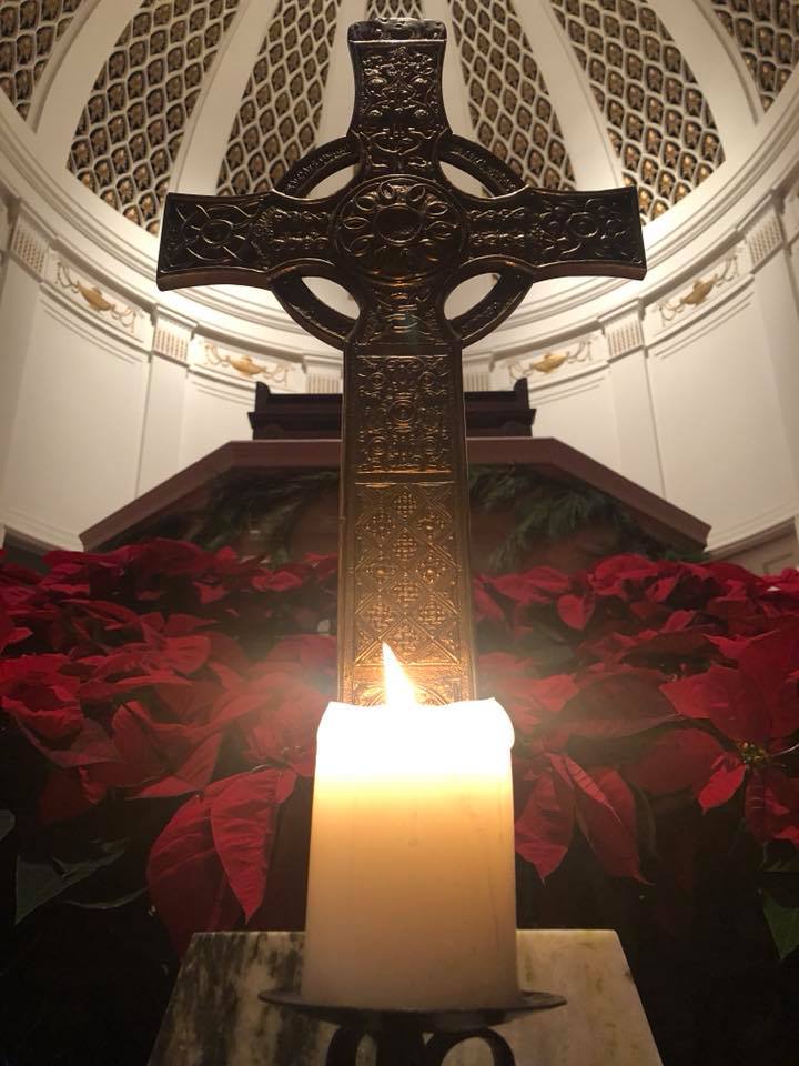 A candle sits in front of the cross and poinsettias