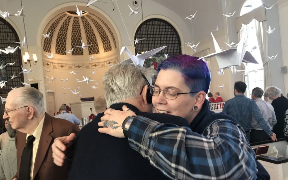 A woman with purple hair hugs a man with white hair