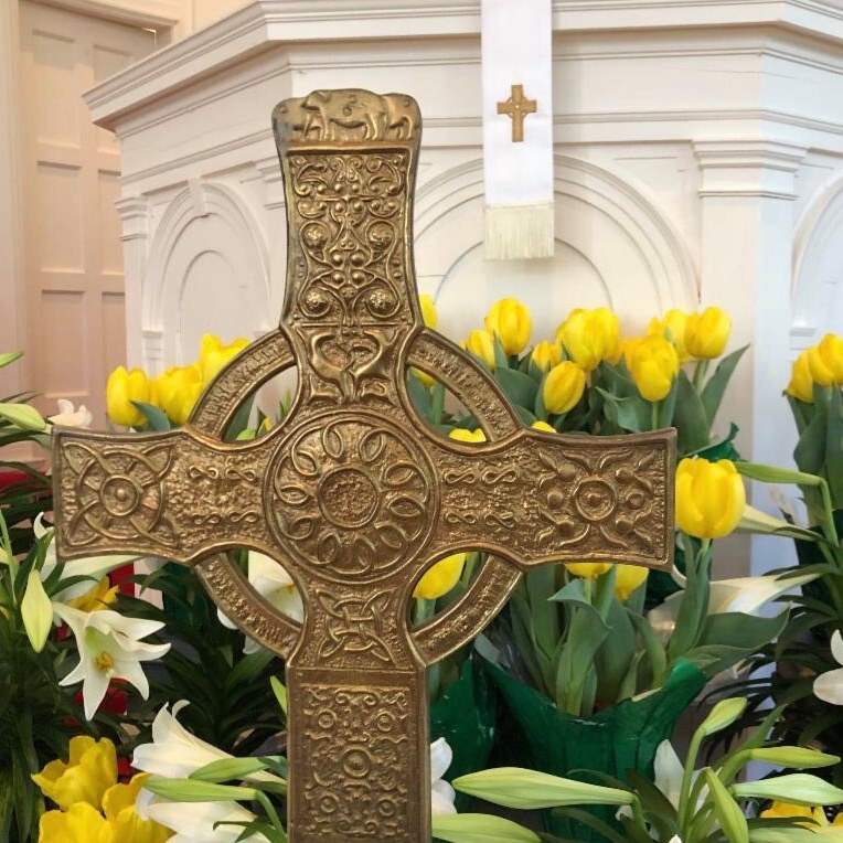 The cross and Easter lilies and tulips sit in front of the pulpit