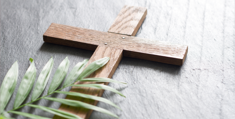 A small wooden cross and a palm leaf are lying on a table.