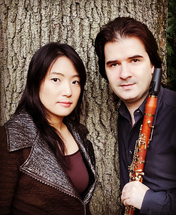 Pianist Misuzu Tanaka and clarinetist Maksim Shtrykov stand in front of a tree trunk