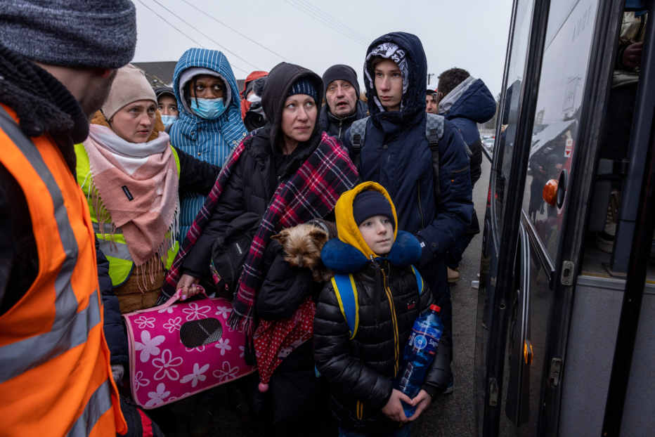 Refugees huddle in cold weather outside bus